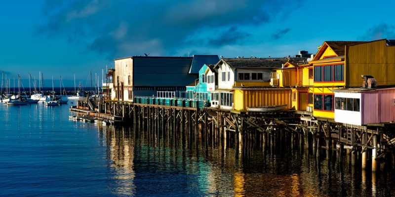 Multicolored buildings built over a wooden pier reflecting on blue water on a cloudy day