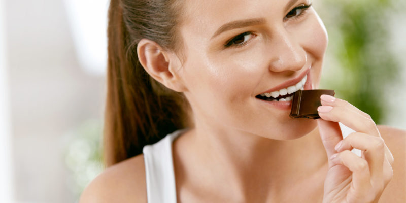 A brown haired woman nibbles a square of dark chocolate