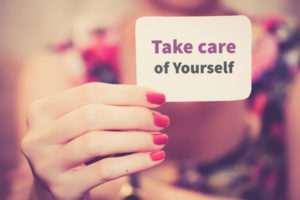 Woman's hand holding a note that says "Take care of yourself"