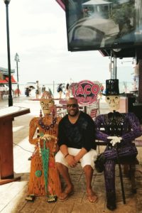 Recruiter Antwan sits centered on an outdoor bench in Cancun with two metal framed skeletons