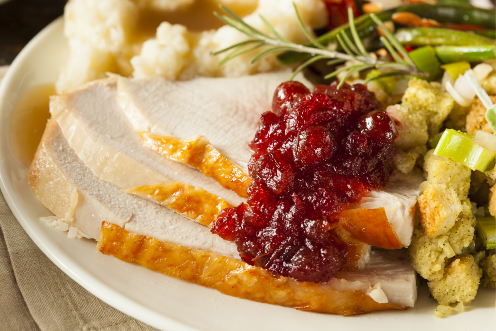 slices of turkey topped with cranberry sauce with mashed potatoes, green beans, and stuffing