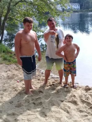 Jason holds a fish while standing in the middle of his two young bathing-suit-cladnephews