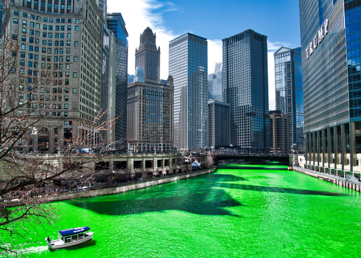 A boat navigates the Chicago River dyed green on a blue sky day. 