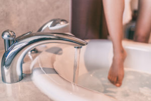 White woman dips barefoot into running bath