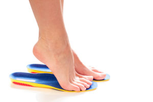 White woman stands tiptoe on red/yellow/blue orthotics