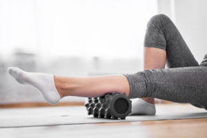 White woman lays supine while using black foam roller on left calf