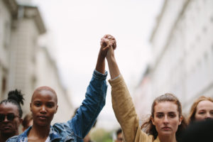 Black and white women hold each others hands above their heads